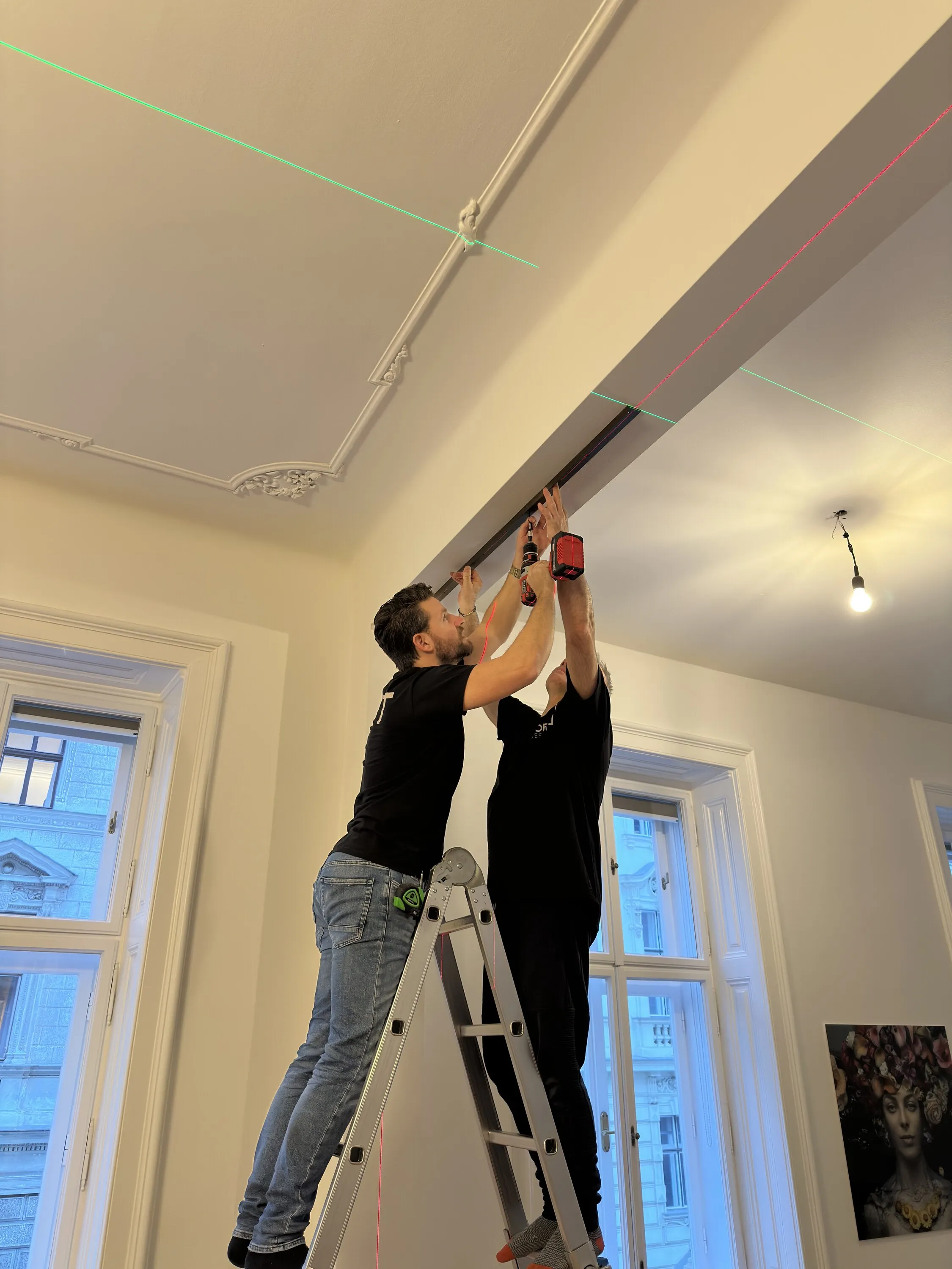 Zwei Monteure befestigen das obere Profil des bronzefarbenen Raumteilers mit Laserlinien in einer Altbauwohnung in Wien