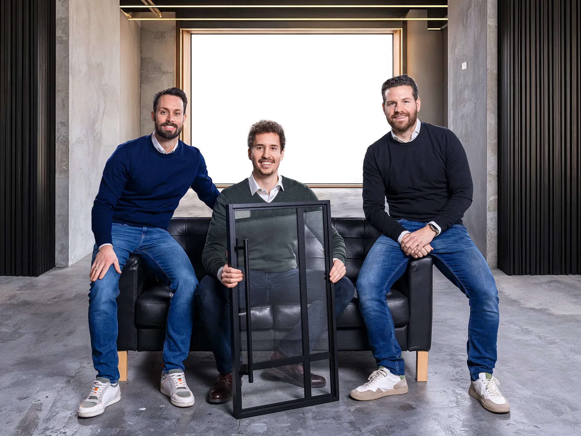 Die drei Gründer von LOFT Design auf einer schwarzen Couch in einem modernen Studio.