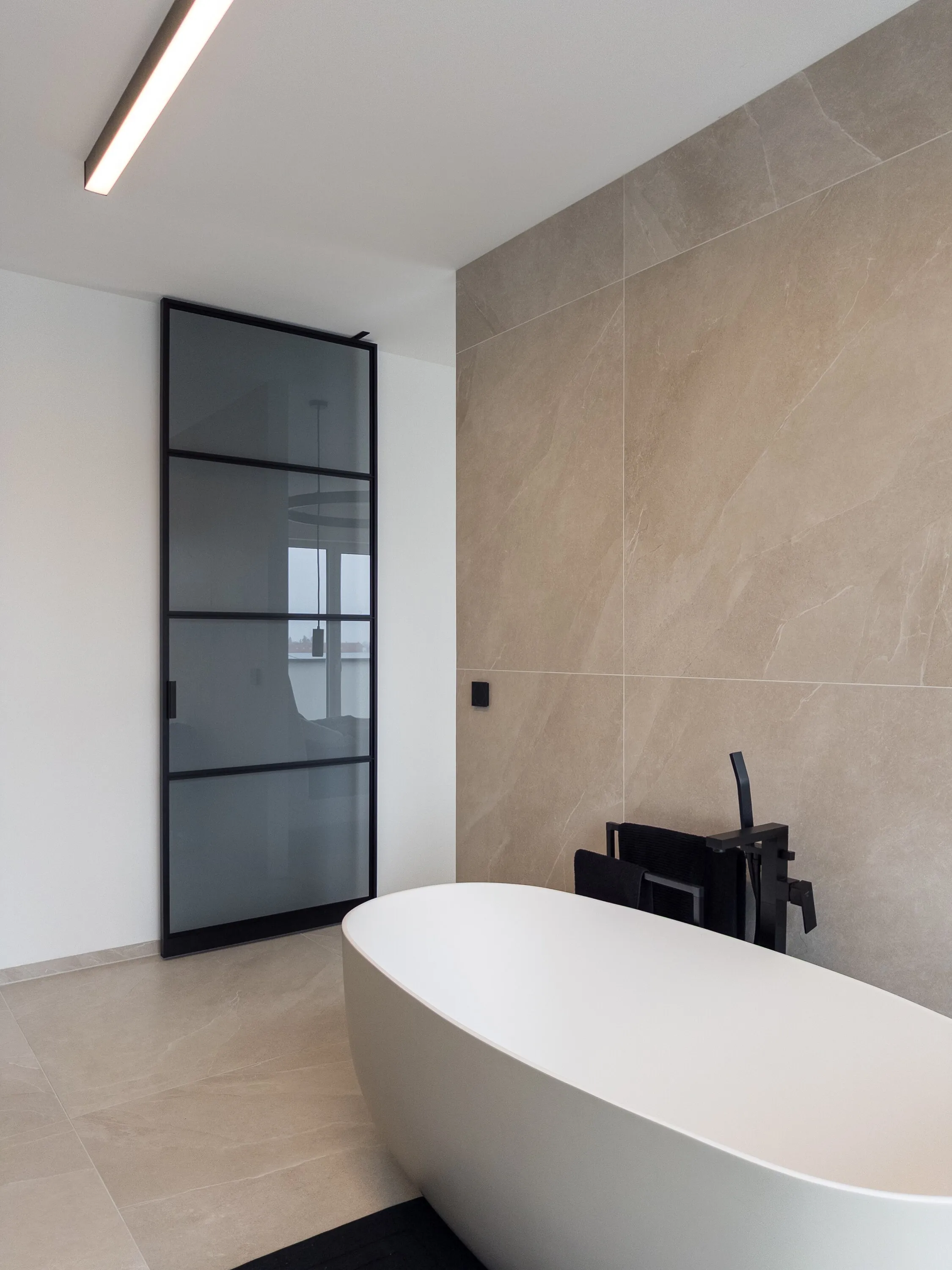 Schwarze Grauglas-Pivottür mit drei horizontalen Sprossen neben einer freistehenden Badewanne in Linz