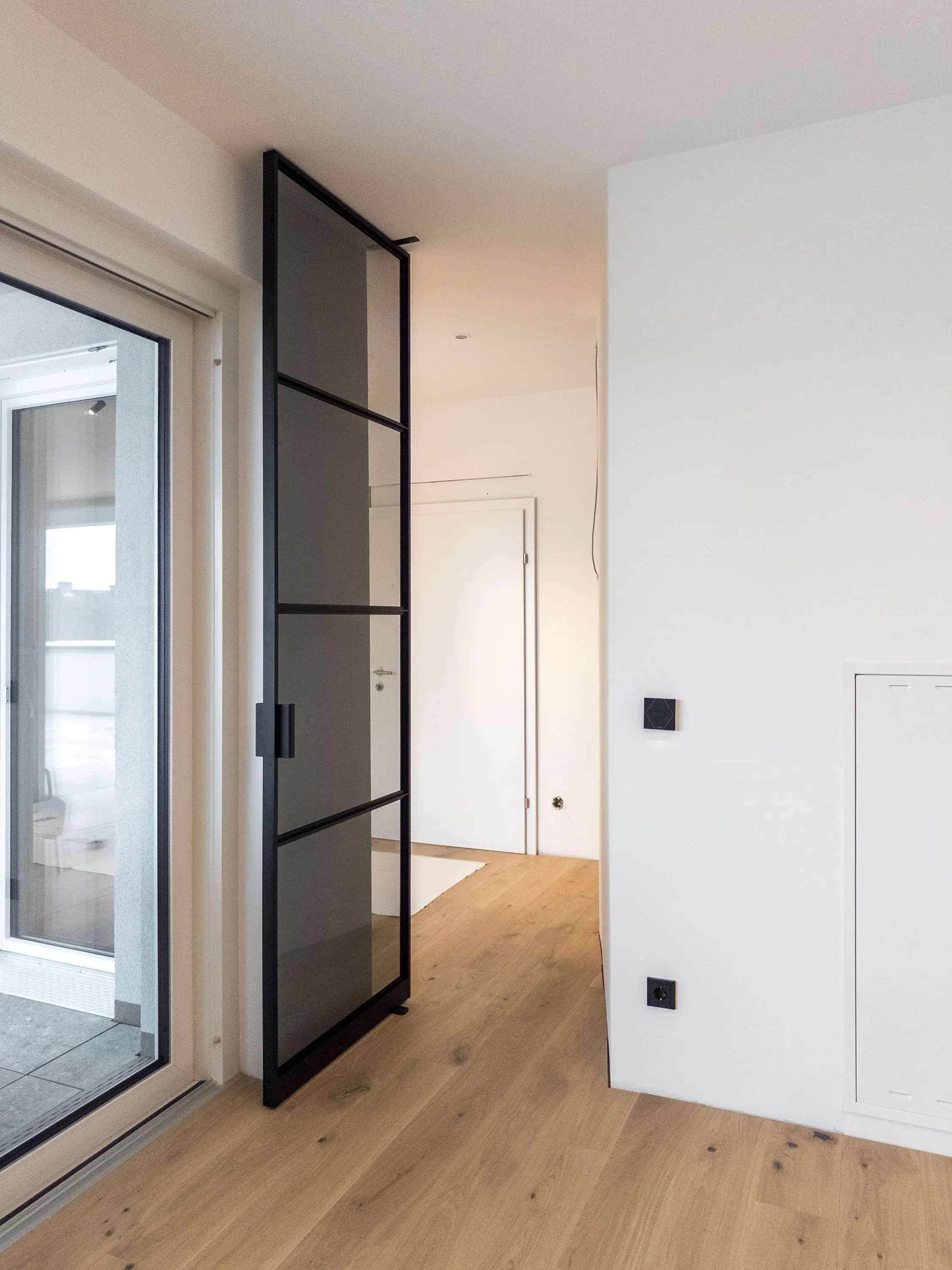 Geöffnete Grauglas-Pivottür mit einseitigem Anschlagsprofil an der schrägen Wand in Enns