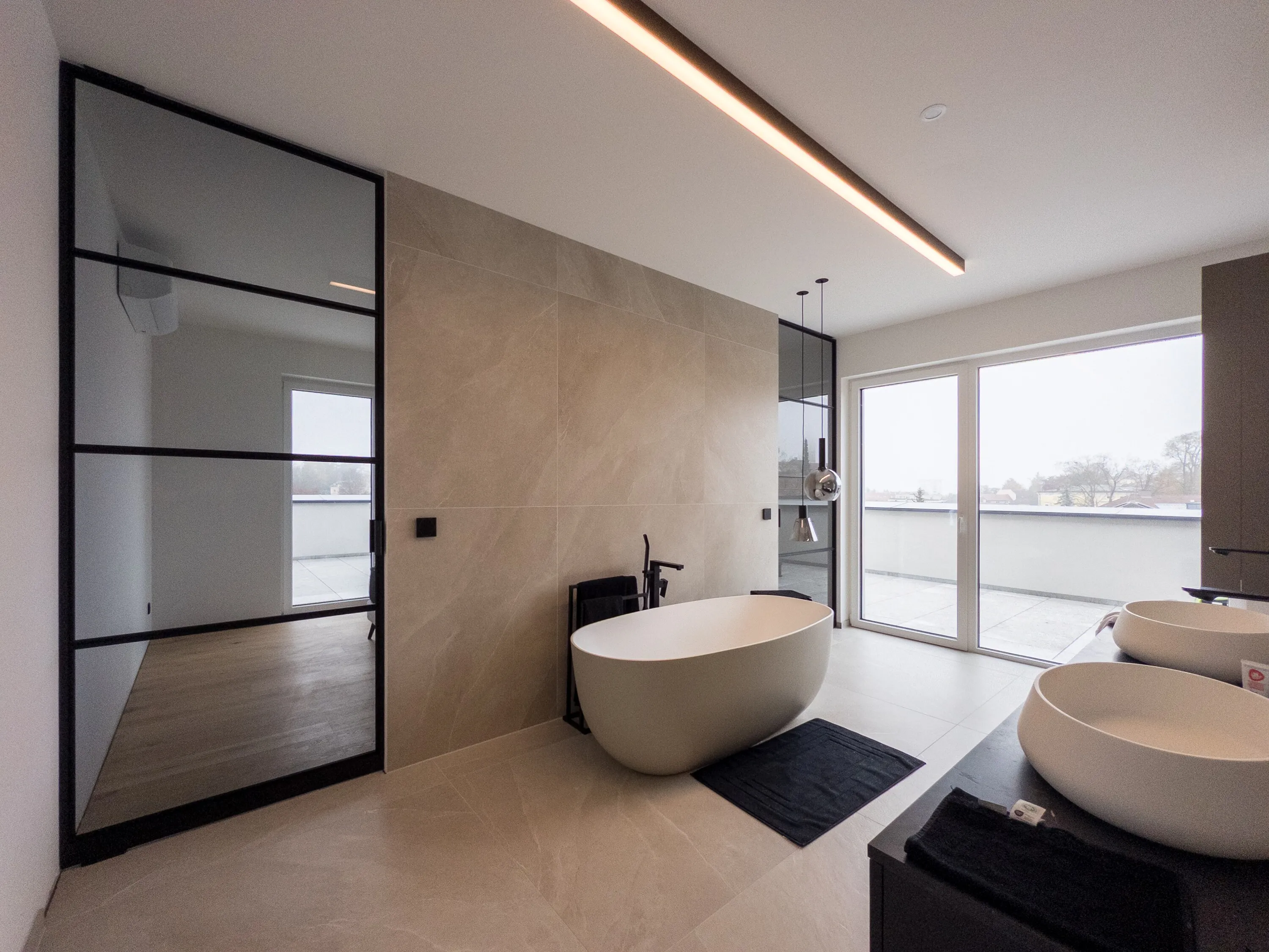 Badezimmer mit freistehender Badewanne und zwei schwarzen Grauglas-Pivottüren vor den Schlafräumen