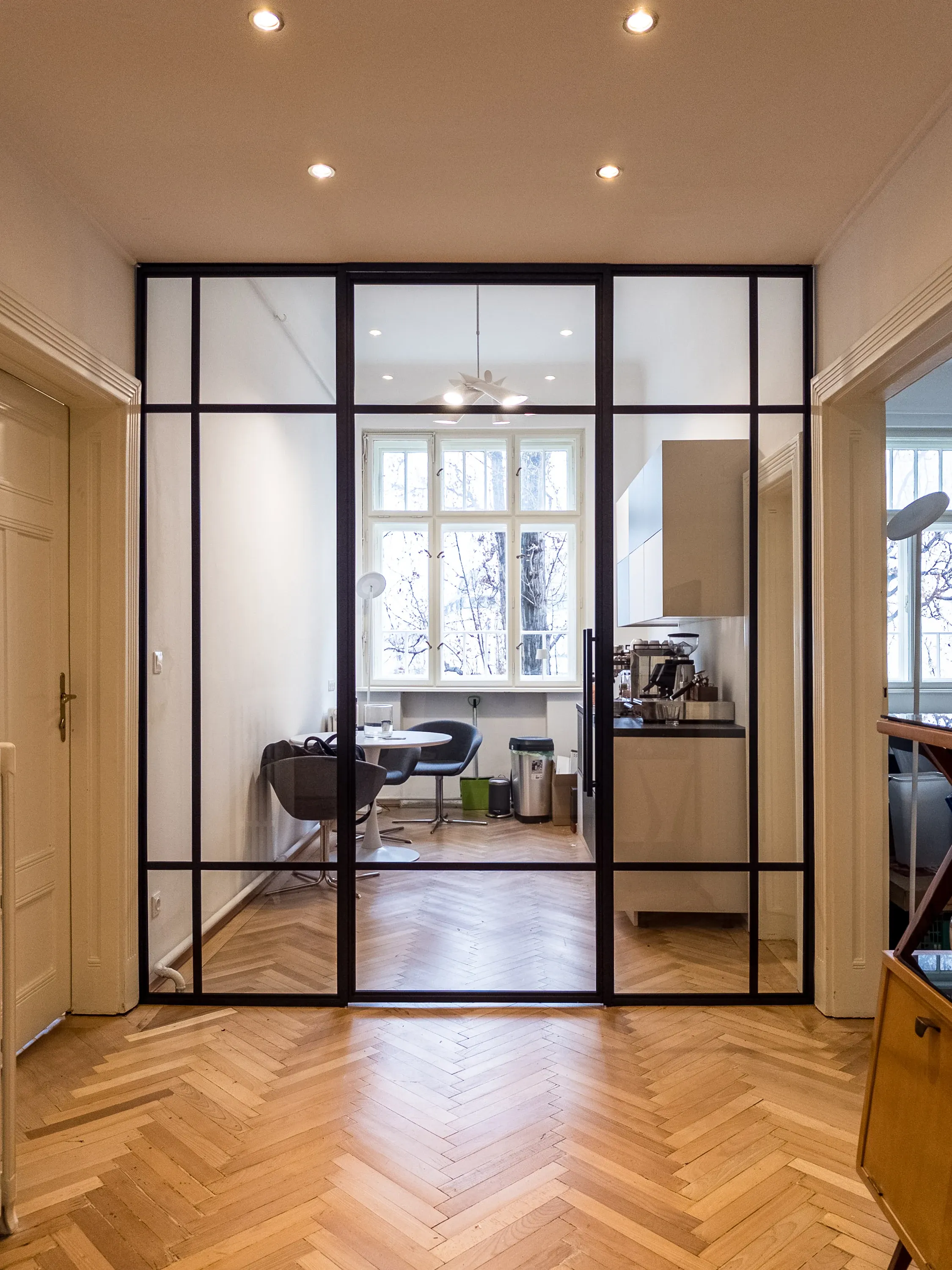 Geschlossene schwarze Glasfront mit Scharniertür und Seitenteilen zur Teeküche im Altbau-Büro