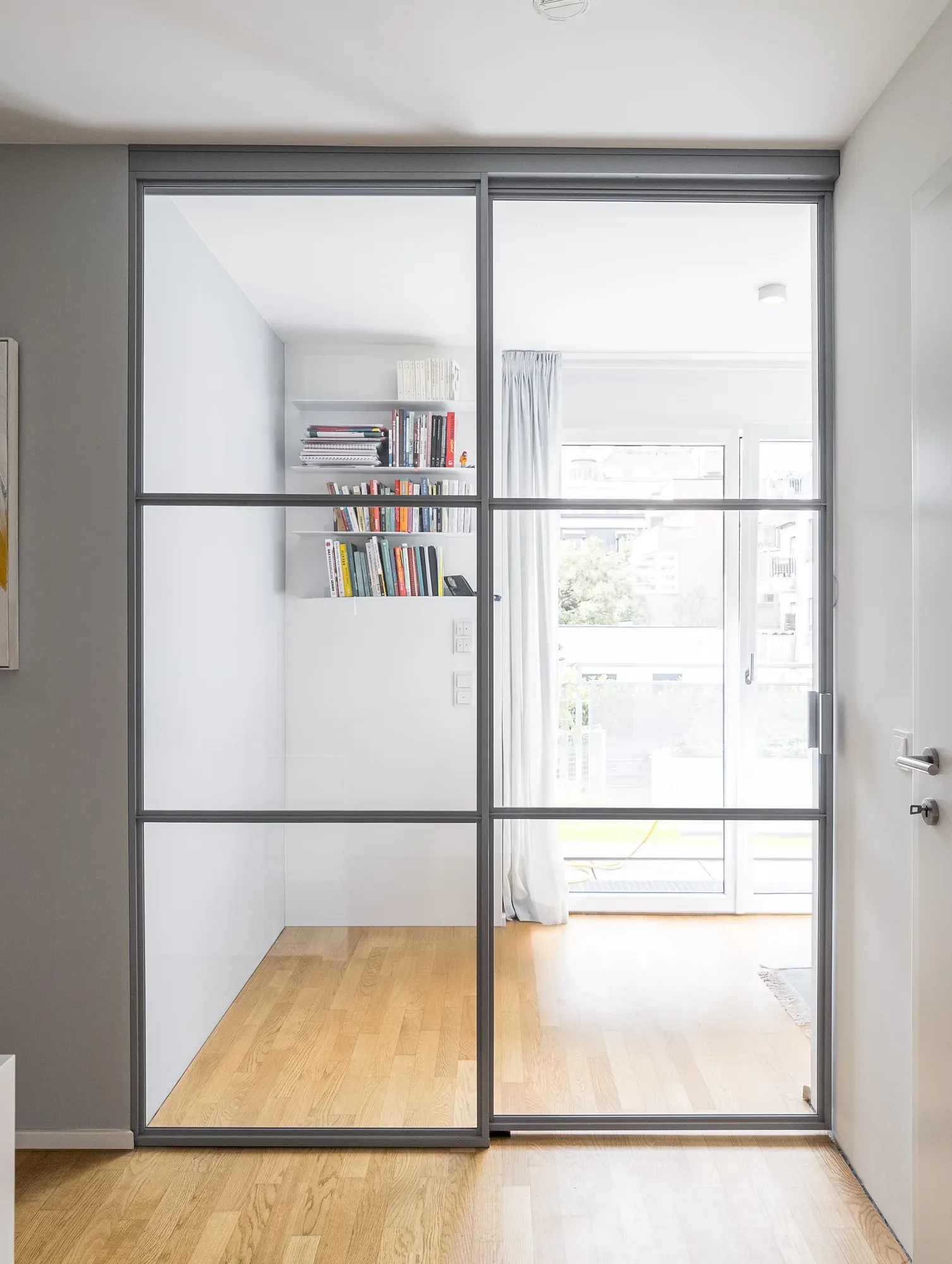Teilweise geöffnete deckenmontierte Schiebetür in RAL 7040 Fenstergrau zwischen Stiegenhaus und Home-Office in Wien