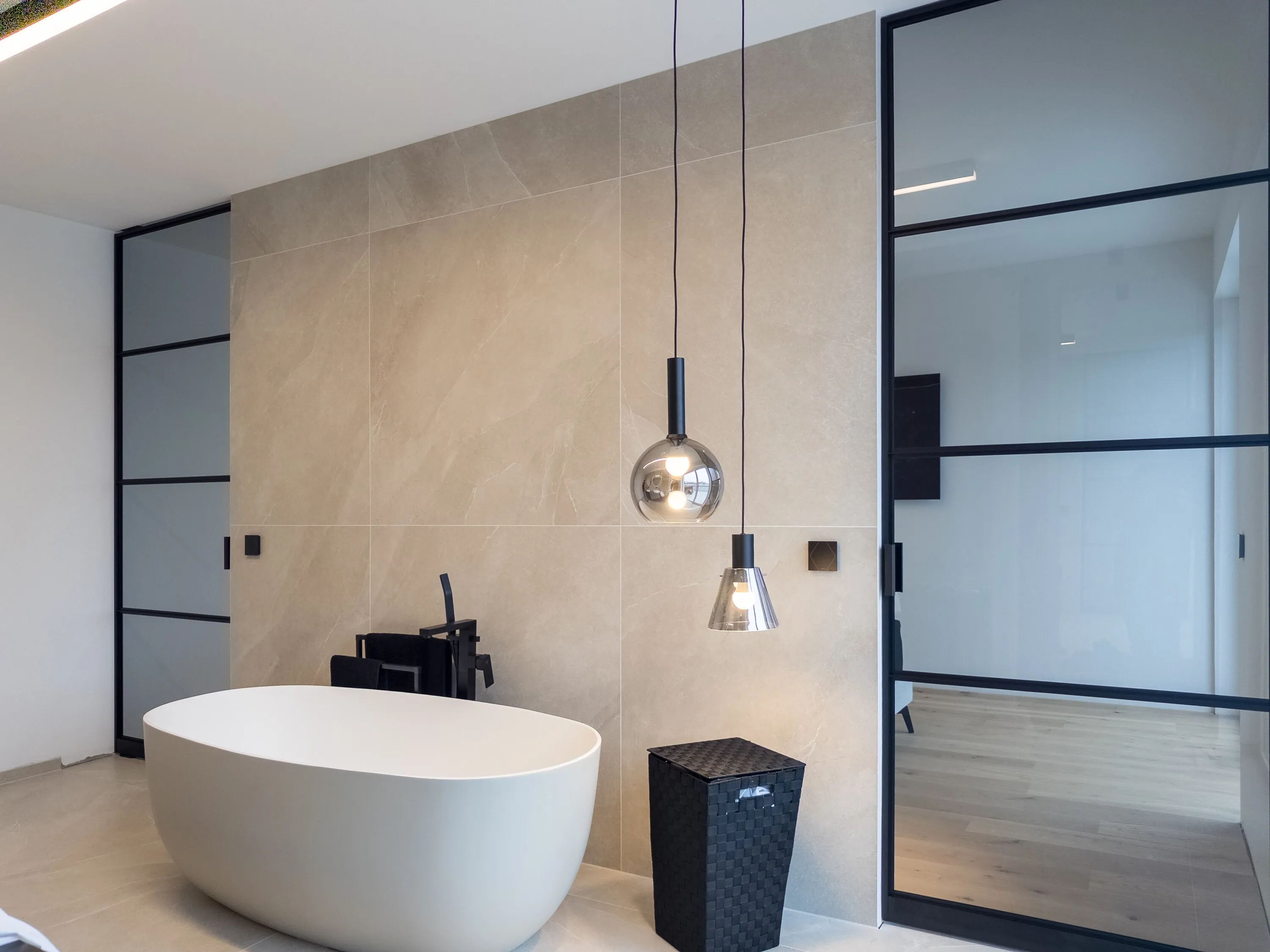 Gesamtansicht des Badezimmers mit zwei schwarzen Grauglas-Pivottüren und freistehender Badewanne in Linz